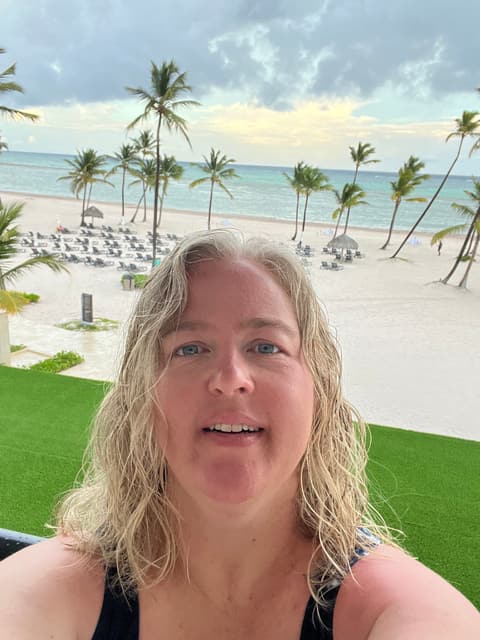 Michelle smiling on her balcony above a palm-lined white-sand beach in Punta Cana