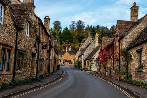 A street lined with honey-stone buildings beside trees in the Cotswolds