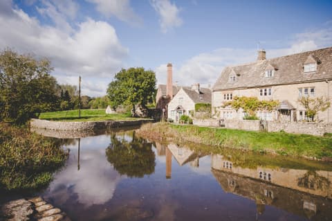 Honey-stone cottages in Lower Slaughter reflected in the stream beside them