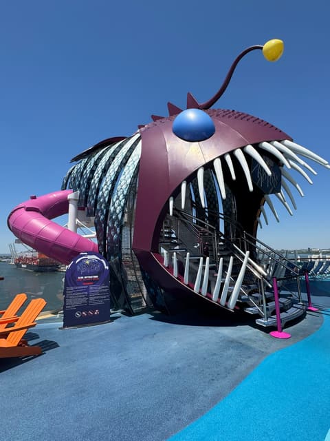 A giant anglerfish-shaped water slide with a glowing lure on the top deck of a cruise ship