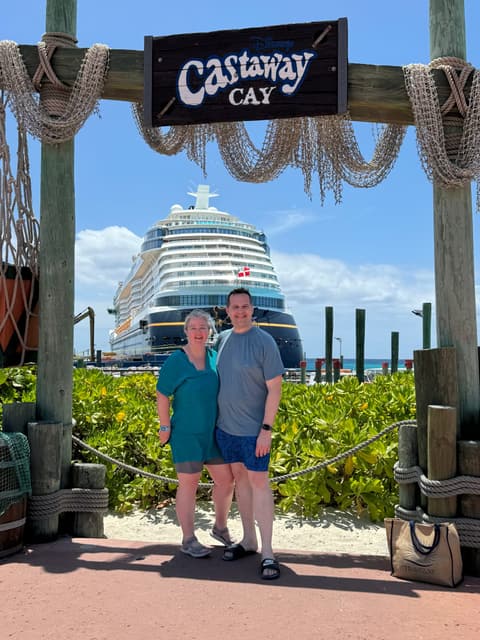 Michelle and her husband under the Castaway Cay sign, with the Disney Wish docked behind them