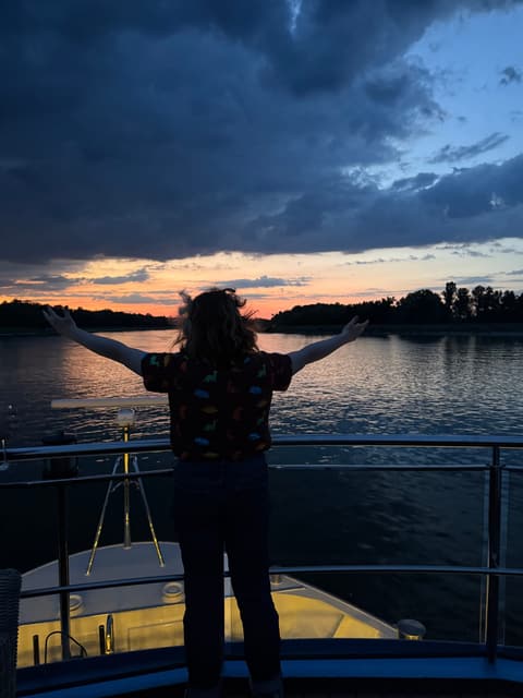 Michelle with her arms spread wide on the bow of a river cruise ship at sunset on the Rhine