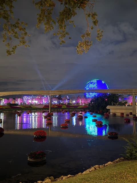 Spaceship Earth glowing with colorful lights over the water at Epcot at night