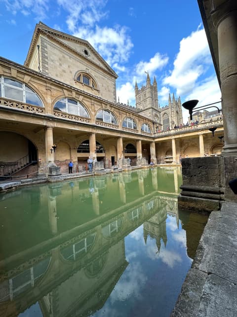 The Roman Baths in Bath, England, with Bath Abbey reflected in the green water